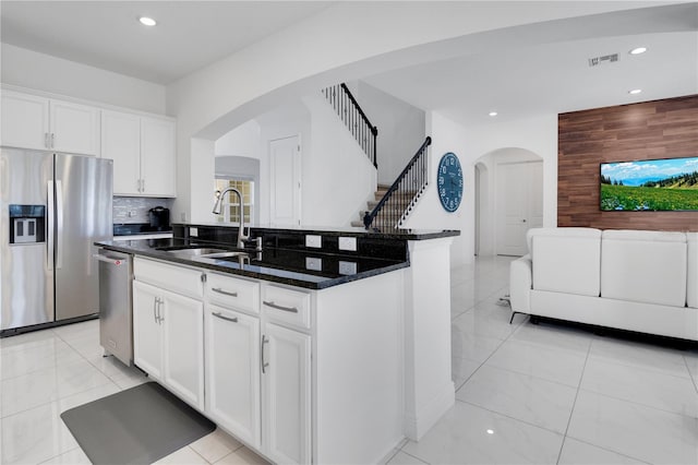 kitchen featuring white cabinetry, sink, stainless steel appliances, an island with sink, and dark stone counters