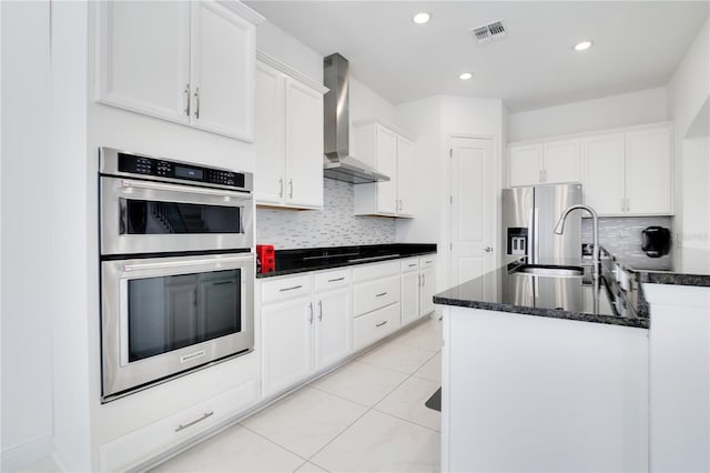 kitchen with appliances with stainless steel finishes, tasteful backsplash, sink, wall chimney range hood, and white cabinets