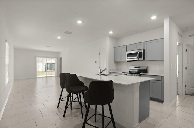 kitchen featuring stainless steel appliances, sink, a center island with sink, and gray cabinets