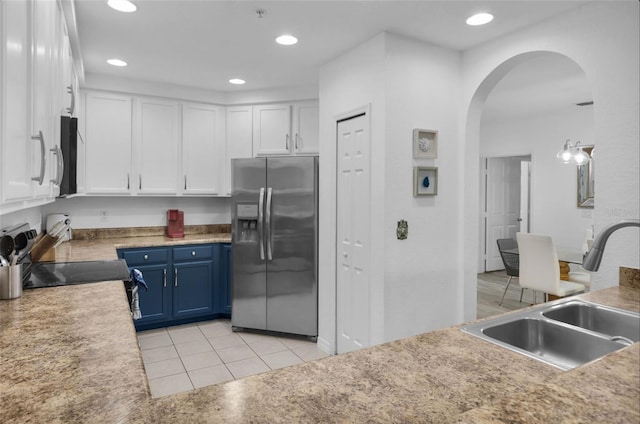 kitchen with stainless steel fridge, sink, blue cabinetry, light tile patterned floors, and white cabinets