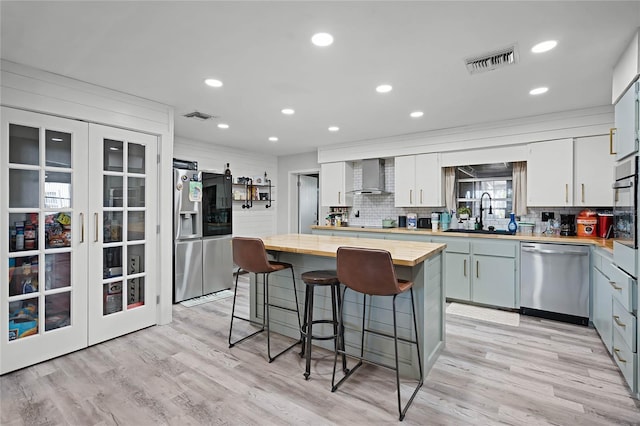 kitchen featuring appliances with stainless steel finishes, wall chimney exhaust hood, sink, a center island, and butcher block countertops