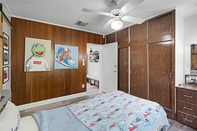 bedroom with light wood-type flooring, wooden walls, ceiling fan, and crown molding