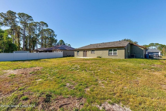 rear view of house with stucco siding, fence, and a yard