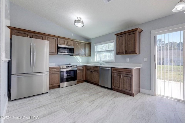 kitchen featuring lofted ceiling, appliances with stainless steel finishes, light countertops, and a sink