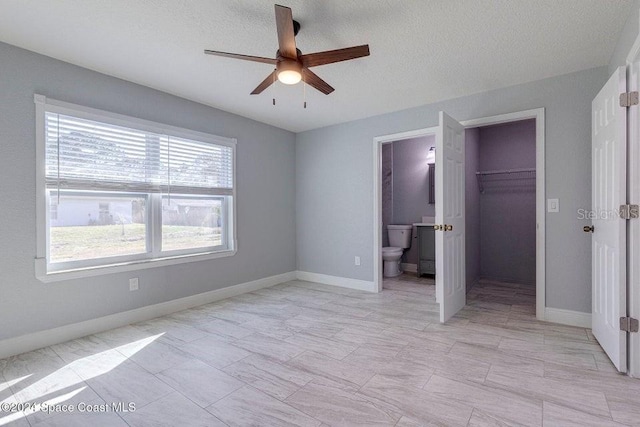 unfurnished bedroom with baseboards, ensuite bath, a walk in closet, a textured ceiling, and a closet