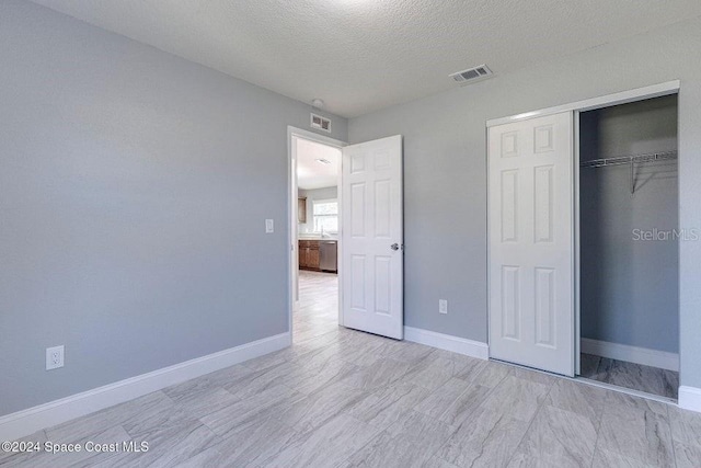 unfurnished bedroom with a textured ceiling, a closet, visible vents, and baseboards