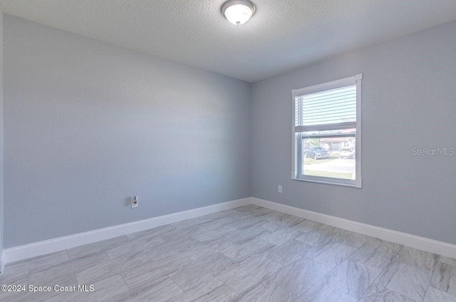 spare room with a textured ceiling and baseboards