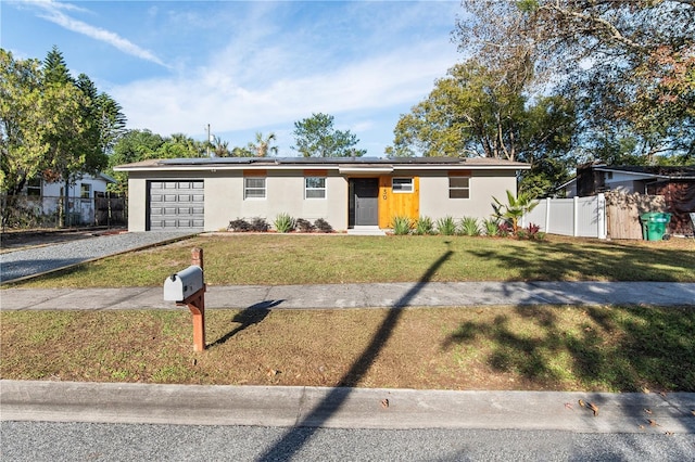 ranch-style house with solar panels, a garage, and a front yard