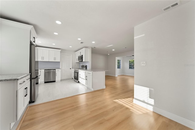 kitchen featuring light stone countertops, stainless steel appliances, white cabinetry, and light hardwood / wood-style flooring