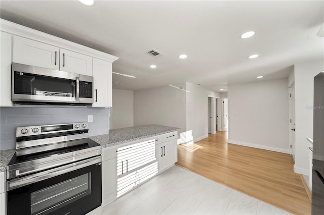 kitchen featuring tasteful backsplash, light stone counters, appliances with stainless steel finishes, white cabinets, and light wood-type flooring