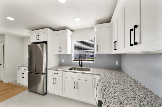 kitchen featuring white cabinetry, sink, stainless steel refrigerator, and tasteful backsplash