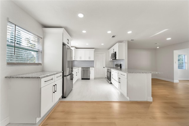 kitchen with kitchen peninsula, white cabinetry, stainless steel appliances, and light stone counters