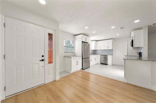 kitchen with sink, light stone counters, light hardwood / wood-style floors, white cabinets, and appliances with stainless steel finishes