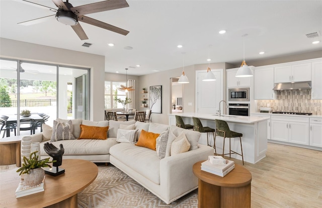 living room featuring ceiling fan, light hardwood / wood-style floors, and sink