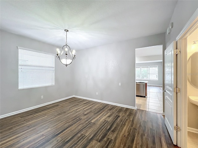 empty room with a notable chandelier and dark hardwood / wood-style floors