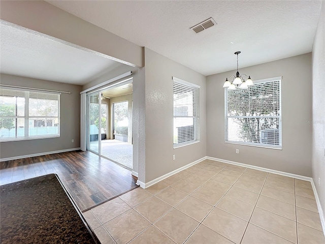 unfurnished dining area with a textured ceiling, ceiling fan with notable chandelier, and light hardwood / wood-style floors