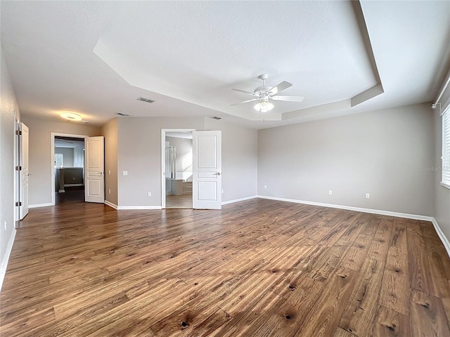 interior space with a tray ceiling, ceiling fan, dark hardwood / wood-style flooring, and ensuite bathroom