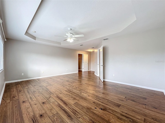 unfurnished room with ceiling fan, a raised ceiling, and dark wood-type flooring