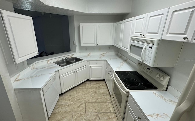 kitchen with light stone counters, white appliances, sink, light tile patterned floors, and white cabinetry