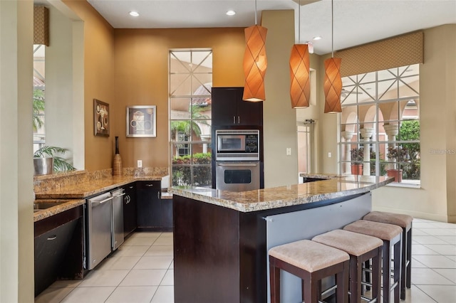 kitchen featuring a kitchen bar, appliances with stainless steel finishes, light stone counters, hanging light fixtures, and light tile patterned flooring