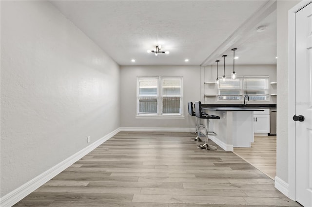 kitchen with a breakfast bar area, white cabinetry, hanging light fixtures, stainless steel dishwasher, and light wood-type flooring