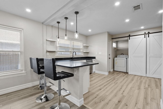 kitchen featuring washing machine and clothes dryer, sink, white cabinetry, decorative light fixtures, and a kitchen breakfast bar