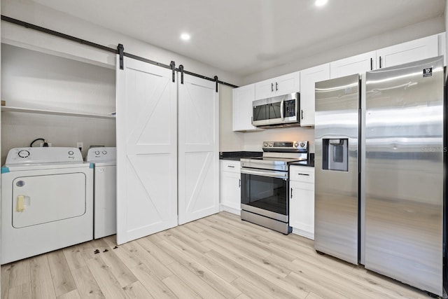 kitchen with appliances with stainless steel finishes, light hardwood / wood-style floors, white cabinets, washing machine and clothes dryer, and a barn door