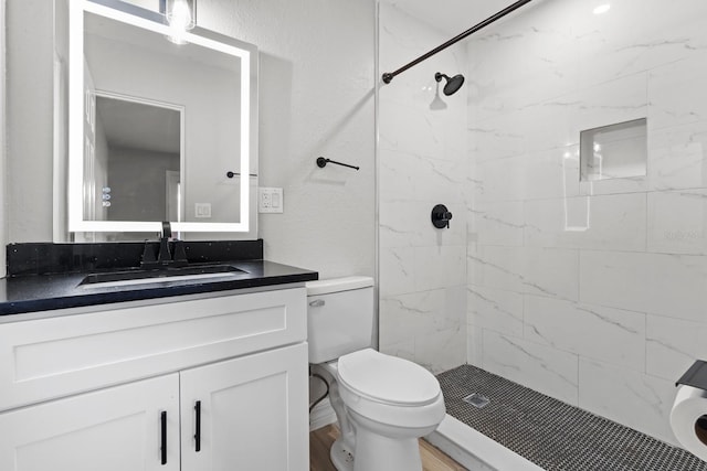 bathroom with vanity, wood-type flooring, a tile shower, and toilet