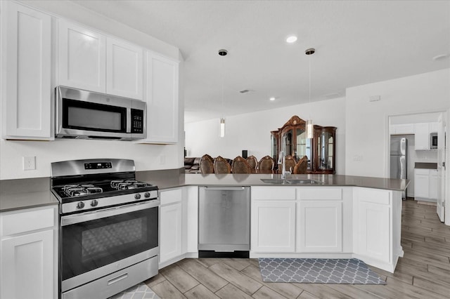 kitchen featuring white cabinetry, sink, stainless steel appliances, kitchen peninsula, and decorative light fixtures