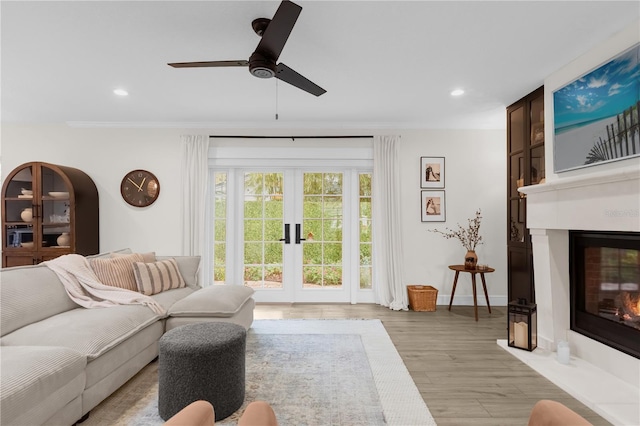 living room with french doors, ceiling fan, ornamental molding, a large fireplace, and light hardwood / wood-style floors