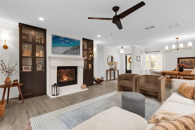 living room with light hardwood / wood-style floors, ceiling fan with notable chandelier, and ornamental molding