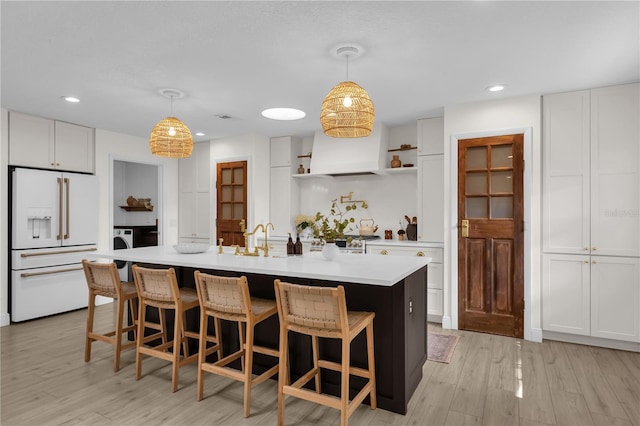 kitchen featuring white cabinetry, white fridge with ice dispenser, hanging light fixtures, and a kitchen island with sink