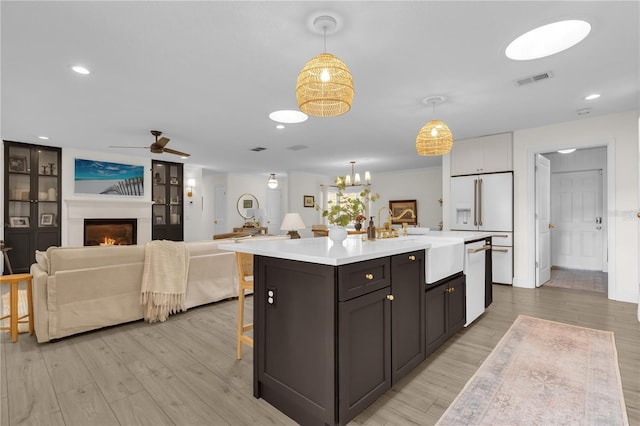 kitchen featuring white appliances, a kitchen island with sink, sink, decorative light fixtures, and light hardwood / wood-style floors