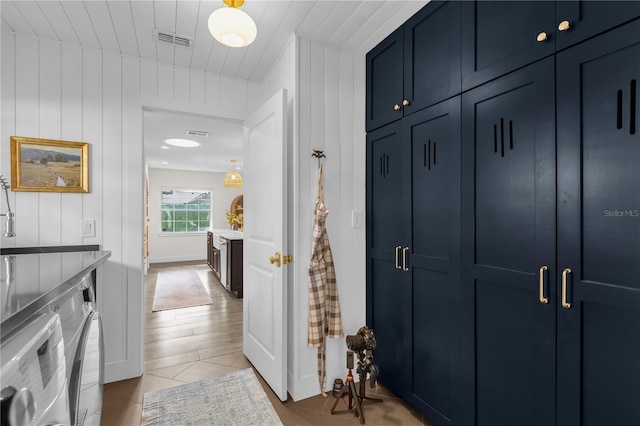 hall with wooden walls, washer and clothes dryer, and light tile patterned floors