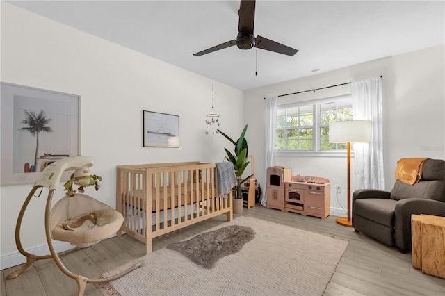 bedroom with light hardwood / wood-style flooring, a nursery area, and ceiling fan