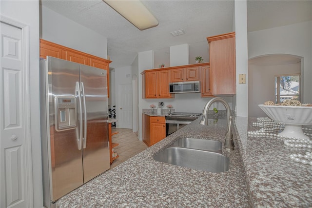 kitchen featuring a textured ceiling, stainless steel appliances, sink, light tile patterned floors, and stone counters