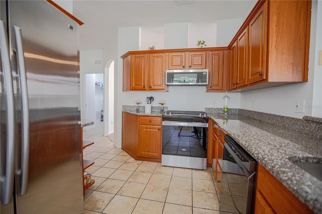 kitchen featuring light tile patterned floors, appliances with stainless steel finishes, and dark stone counters