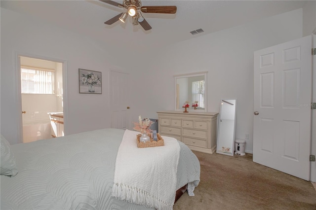 bedroom featuring ceiling fan, multiple windows, light colored carpet, and ensuite bath