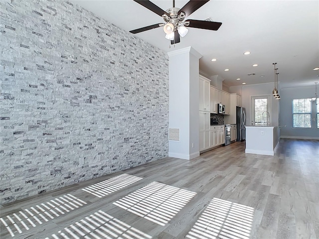 unfurnished living room with light wood-type flooring, ceiling fan, and sink