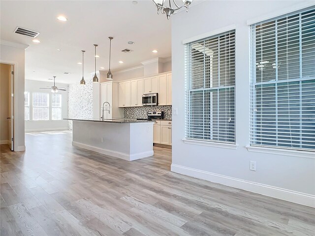 kitchen featuring backsplash, a center island with sink, white cabinets, crown molding, and decorative light fixtures