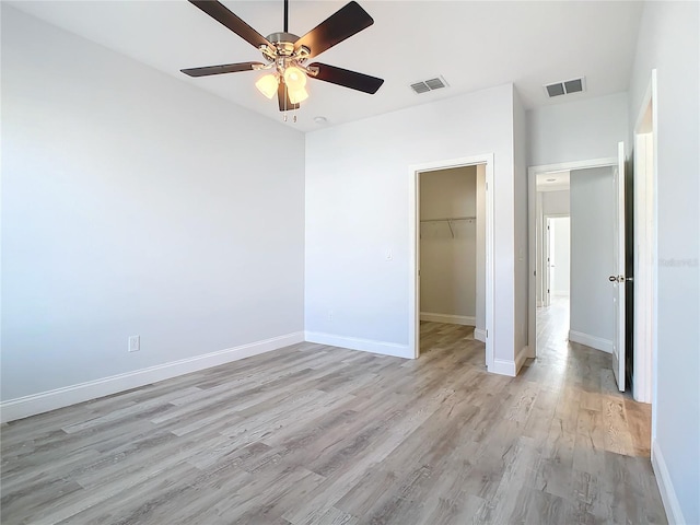 unfurnished bedroom featuring a closet, ceiling fan, light hardwood / wood-style flooring, and a spacious closet