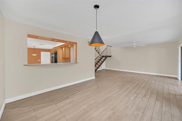 unfurnished living room featuring a textured ceiling, ceiling fan, and light wood-type flooring