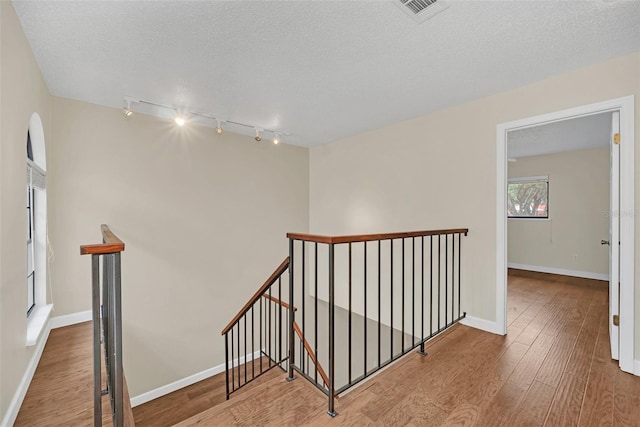 staircase with wood-type flooring, track lighting, and a textured ceiling