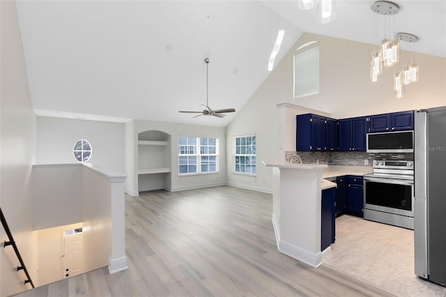 kitchen with high vaulted ceiling, blue cabinets, decorative backsplash, ceiling fan with notable chandelier, and appliances with stainless steel finishes