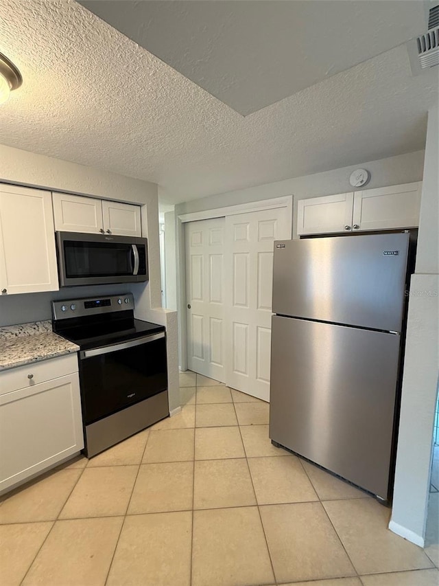 kitchen featuring white cabinetry, light stone counters, a textured ceiling, light tile patterned flooring, and appliances with stainless steel finishes