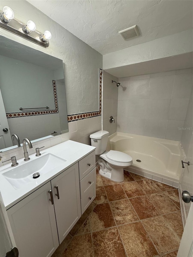 bathroom with a tile shower, tasteful backsplash, a textured ceiling, vanity, and tile walls