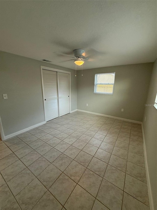 unfurnished bedroom with light tile patterned floors, a textured ceiling, a closet, and ceiling fan