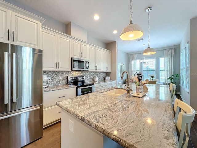 kitchen featuring decorative backsplash, light stone counters, stainless steel appliances, sink, and hanging light fixtures