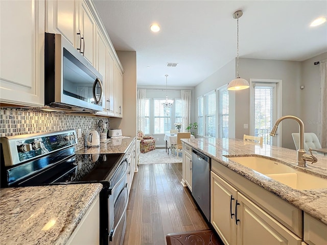 kitchen with backsplash, stainless steel appliances, sink, pendant lighting, and a notable chandelier