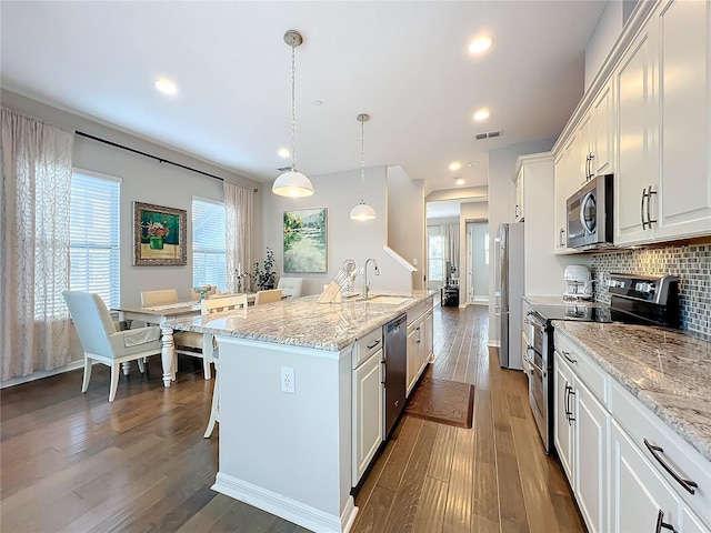 kitchen featuring tasteful backsplash, stainless steel appliances, pendant lighting, a center island with sink, and white cabinetry